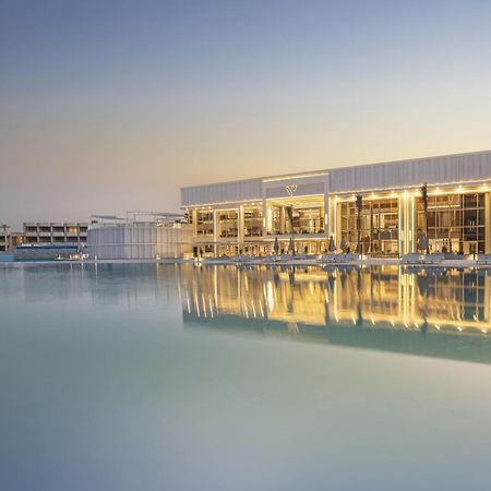 V Hotel Sharm El Shiekh Exterior photo The photo depicts a modern building situated by a calm body of water, likely a lake or lagoon. The structure features a sleek design with large glass windows that reflect the water and the surrounding environment. The setting appears tranquil, possib
