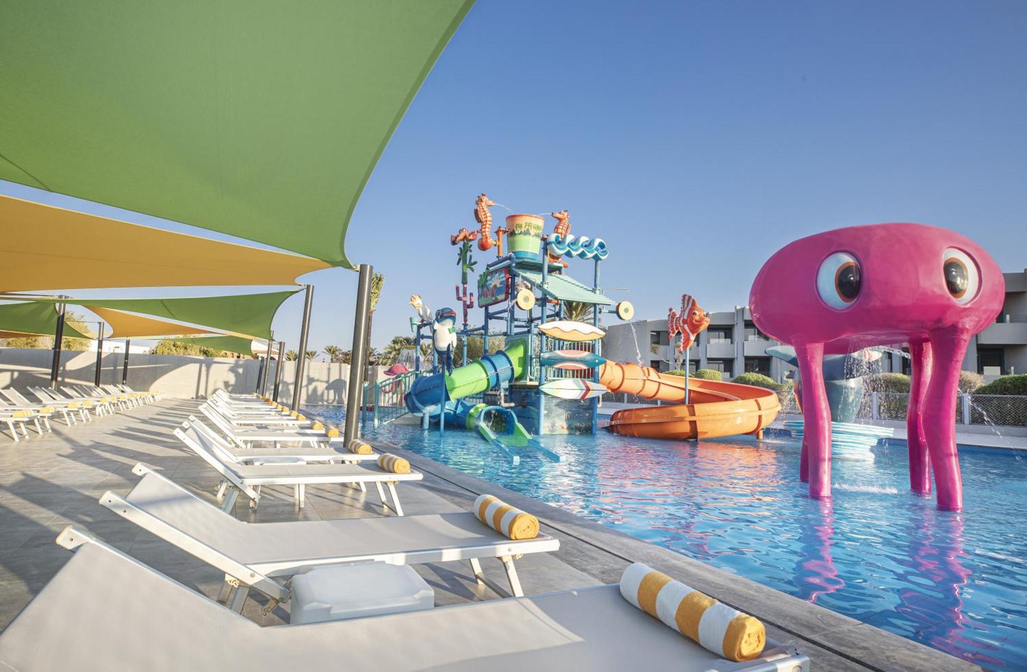 V Hotel Sharm El Shiekh Exterior photo The photo depicts a vibrant pool area designed for enjoyment, featuring colorful water slides and playful aquatic structures. Prominent in the scene is a large pink octopus and various water slides, which suggest a fun-filled environment, likely aime
