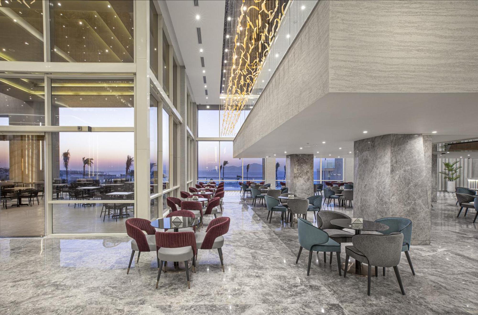 V Hotel Sharm El Shiekh Exterior photo The photo showcases a modern dining space or lounge area featuring large windows that provide a view of the outdoors, likely overlooking a scenic landscape or waterfront. The interior design includes elegant marble flooring and stylish furniture, com