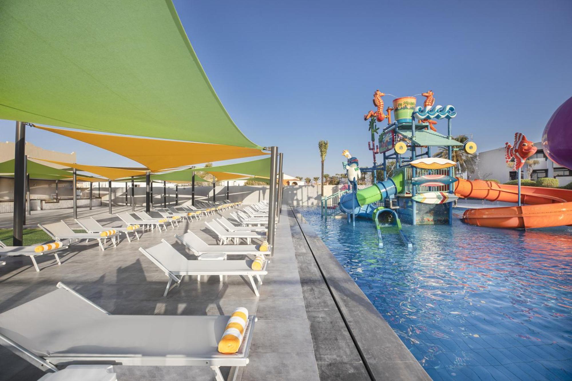 V Hotel Sharm El Shiekh Exterior photo The photo shows a vibrant pool area designed for relaxation and fun. On one side, there are several lounge chairs arranged neatly, featuring colorful towels. The pool itself is clear and inviting, with shades of blue. In the background, there's a lar