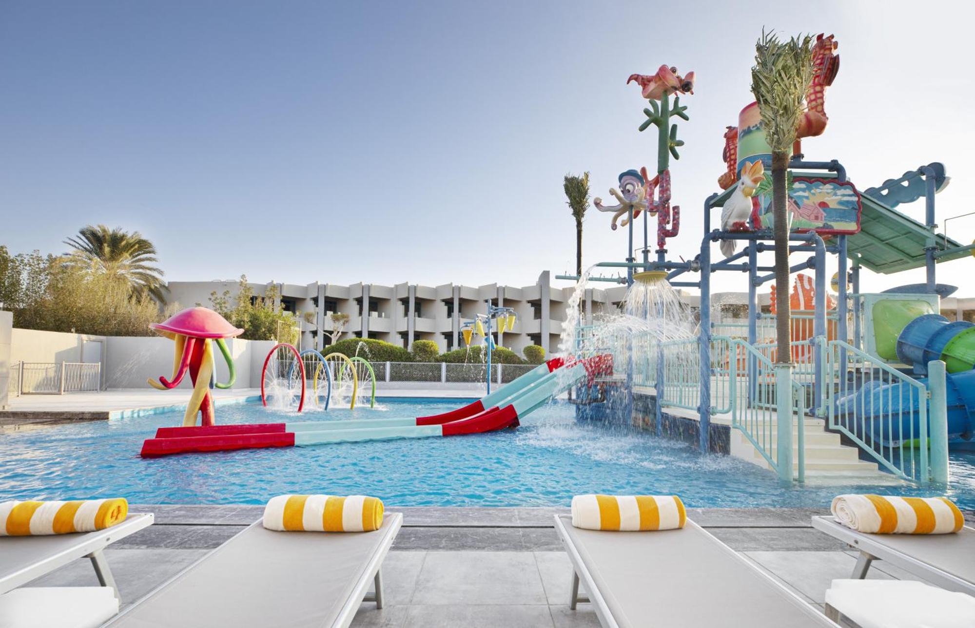 V Hotel Sharm El Shiekh Exterior photo The photo shows a vibrant and colorful water park area. There is a large swimming pool with various water features, including slides and spray elements. The pool area is decorated with bright, playful designs, such as sea creatures and tropical theme