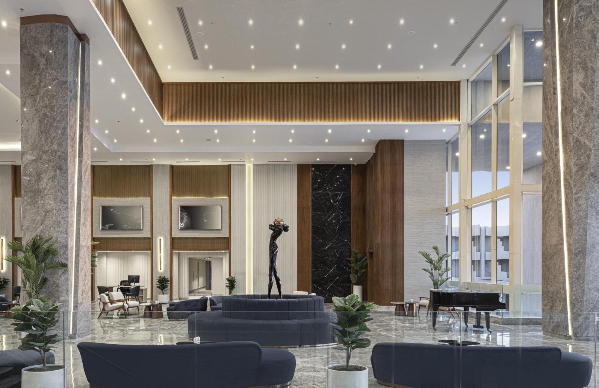 V Hotel Sharm El Shiekh Exterior photo The photo shows a spacious and modern hotel lobby characterized by elegant design features. There are plush, dark blue sofas arranged in a conversational setting, accompanied by stylish chairs. The space is well-lit with numerous ceiling lights, and 