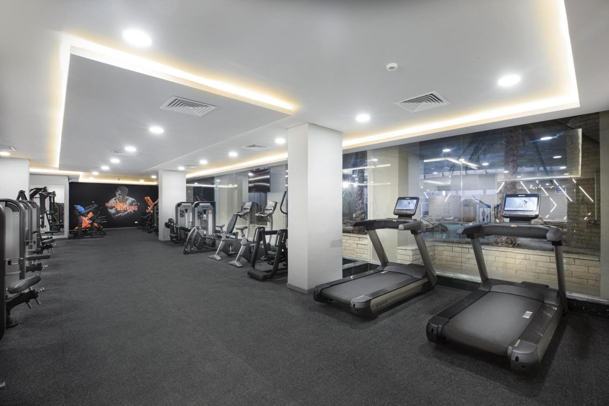 V Hotel Sharm El Shiekh Exterior photo The photo shows a modern gym interior featuring several workout machines and equipment. On the right, there are two treadmills, and on the left, there are various other fitness machines. The space is well-lit with a clean and contemporary design, fea