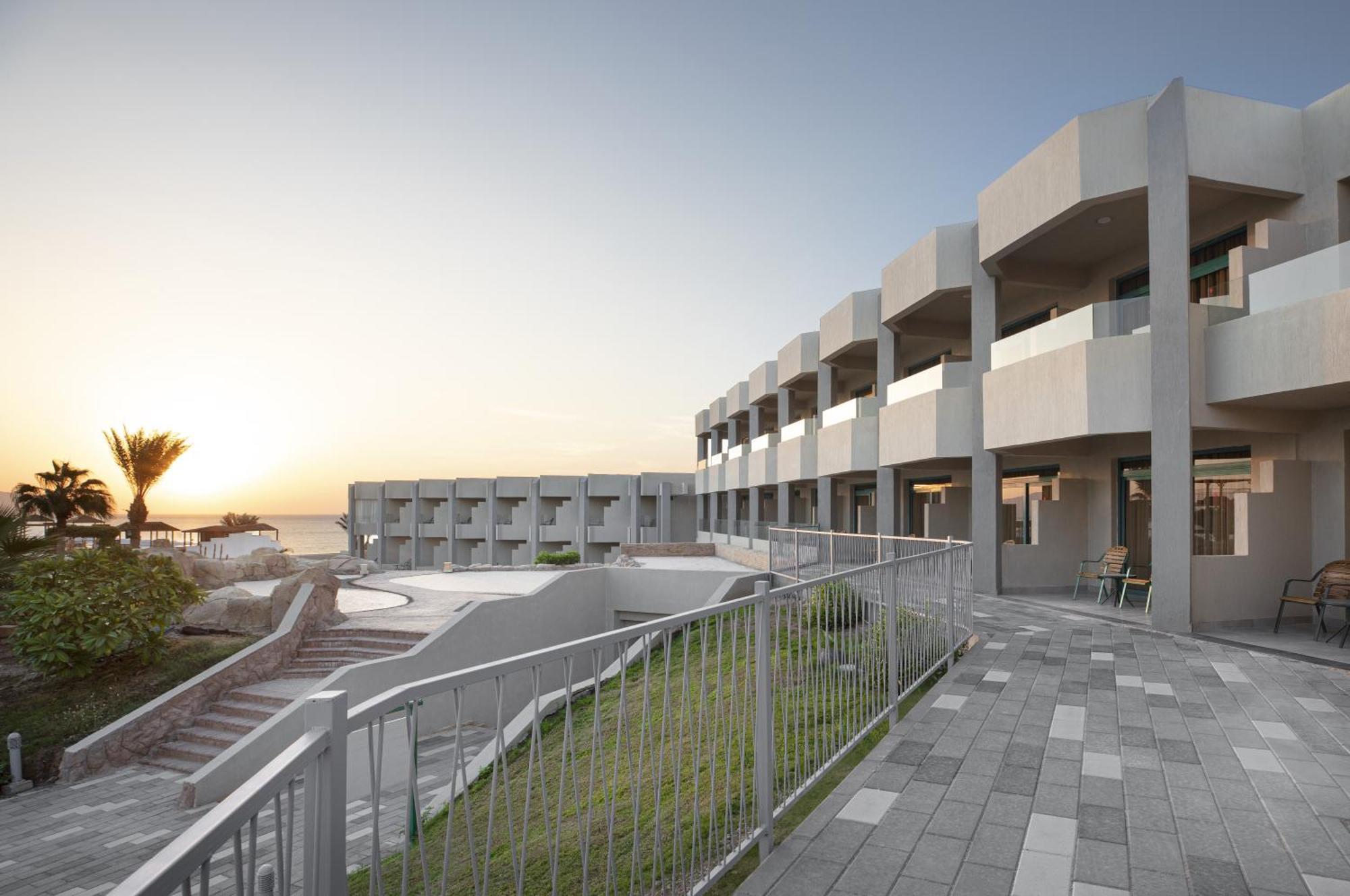V Hotel Sharm El Shiekh Exterior photo The photo shows a modern coastal building with a clean, geometric design. The structure features several levels with balconies, suggesting that it is likely a hotel or resort. In the foreground, there is a landscaped area with a paved walkway and a r