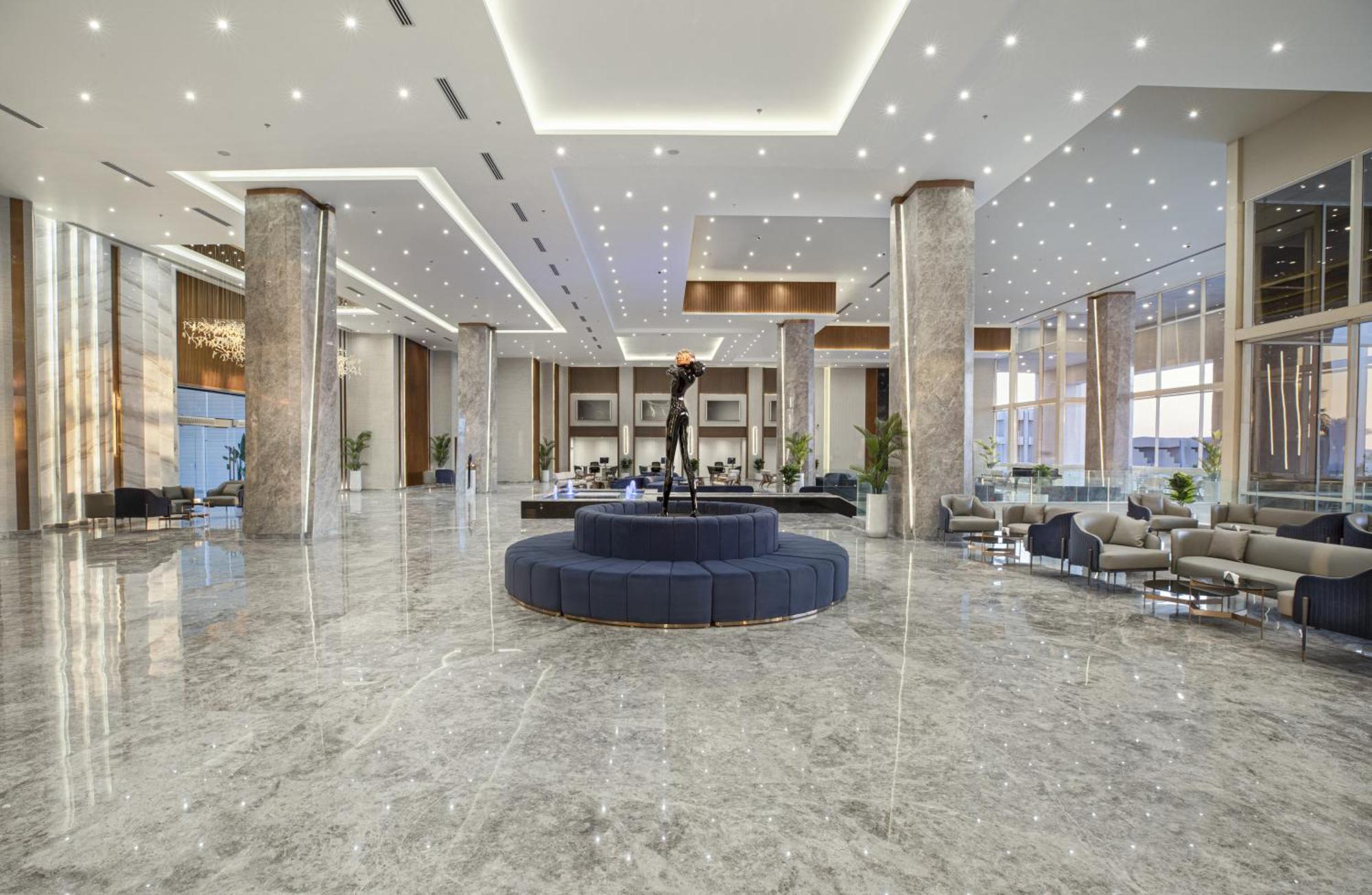 V Hotel Sharm El Shiekh Exterior photo The image shows a spacious and modern lobby area. It features polished marble flooring that reflects the bright overhead lights. The lobby has tall pillars, large windows allowing for natural light, and an elegant design. In the center, there is a ci