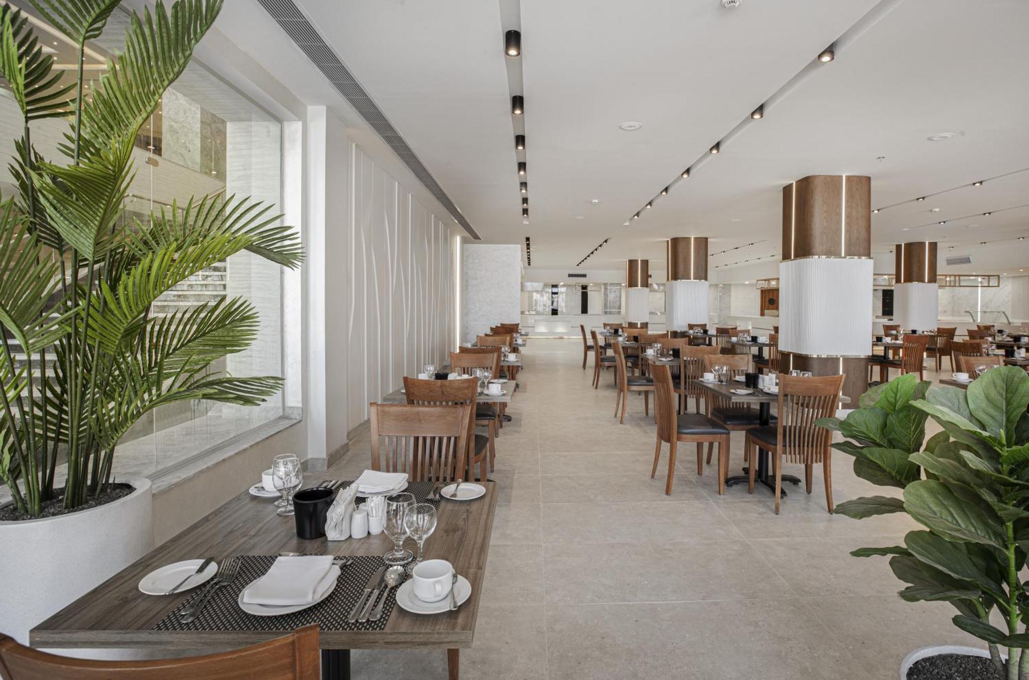 V Hotel Sharm El Shiekh Exterior photo The photo shows the interior of a modern dining area, likely a restaurant or a café. The space features a clean, contemporary design with wooden furniture, including dining tables and chairs. Each table is set with plates, glasses, and utensils, sugg