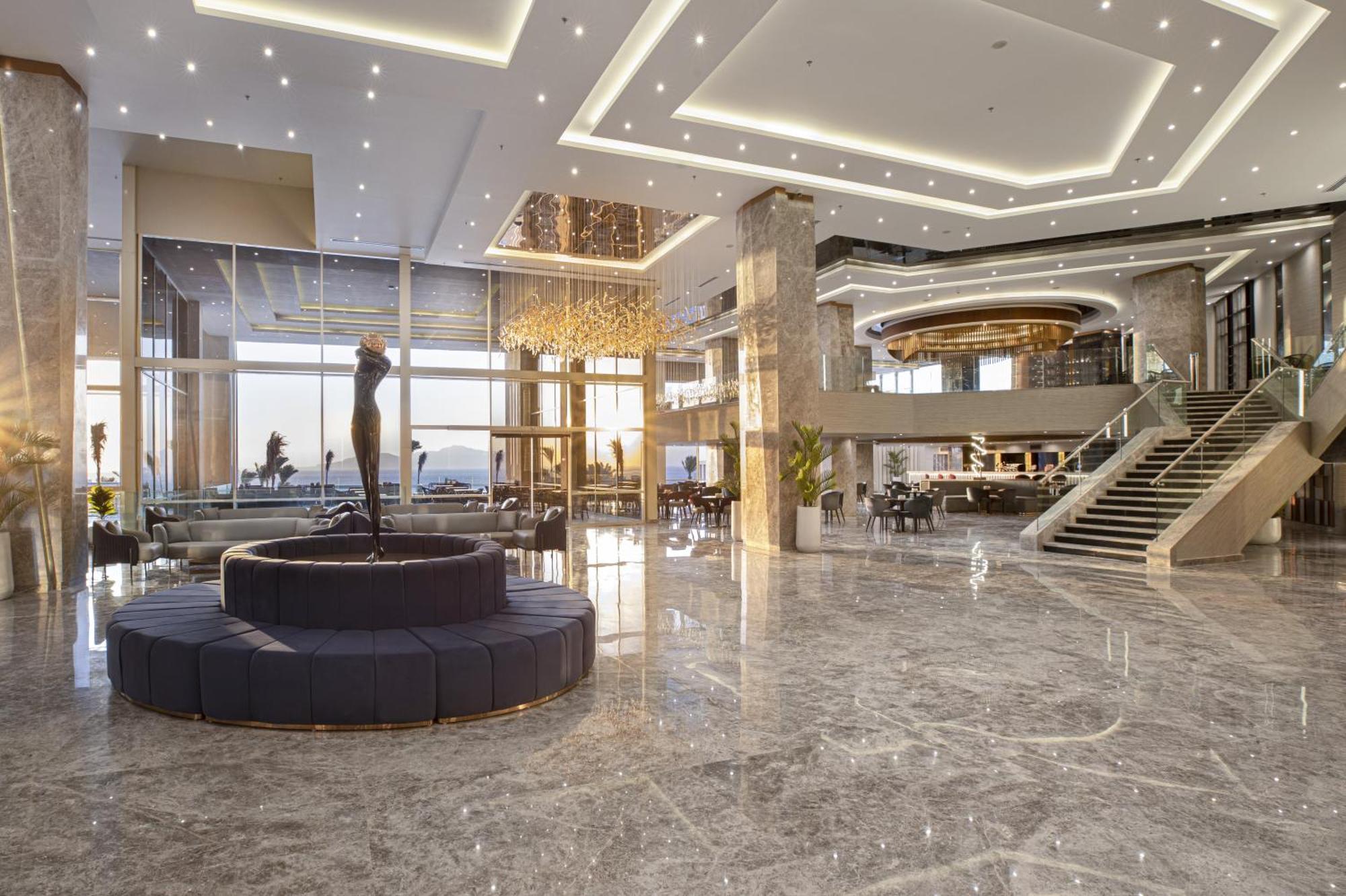 V Hotel Sharm El Shiekh Exterior photo The photo showcases an elegant hotel lobby with modern architecture and design. The space features a high ceiling illuminated by a combination of recessed lights and decorative fixtures. A prominent marble floor adds to the luxurious atmosphere, and 