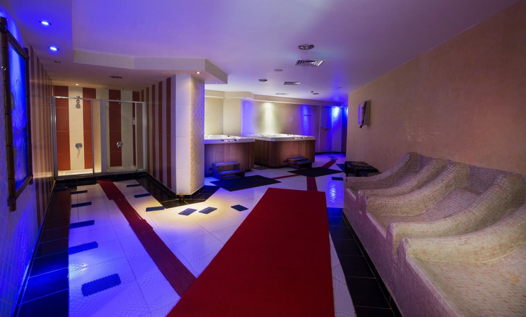 V Hotel Sharm El Shiekh Exterior photo The photo shows a modern interior space, likely a luxurious spa or relaxation area. It features a well-lit corridor with soft blue lighting. There is a red carpet leading down the center, bordered by black and white tile patterns. On one side, there 