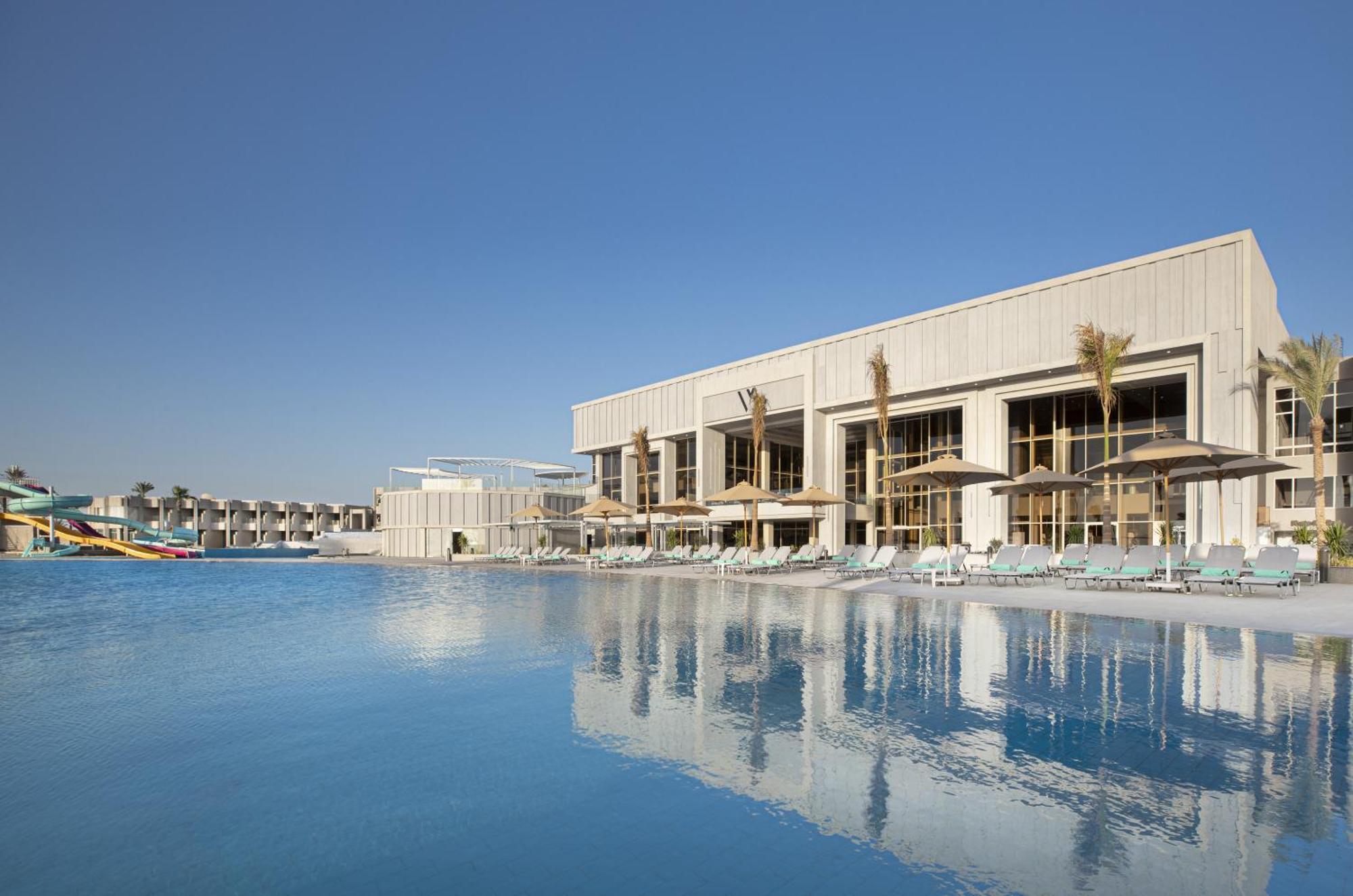 V Hotel Sharm El Shiekh Exterior photo The photo shows a modern building adjacent to a swimming pool. The pool has a clear blue surface reflecting the sky and the structure. The building features large windows and is designed with a minimalist aesthetic, complemented by palm trees. There 