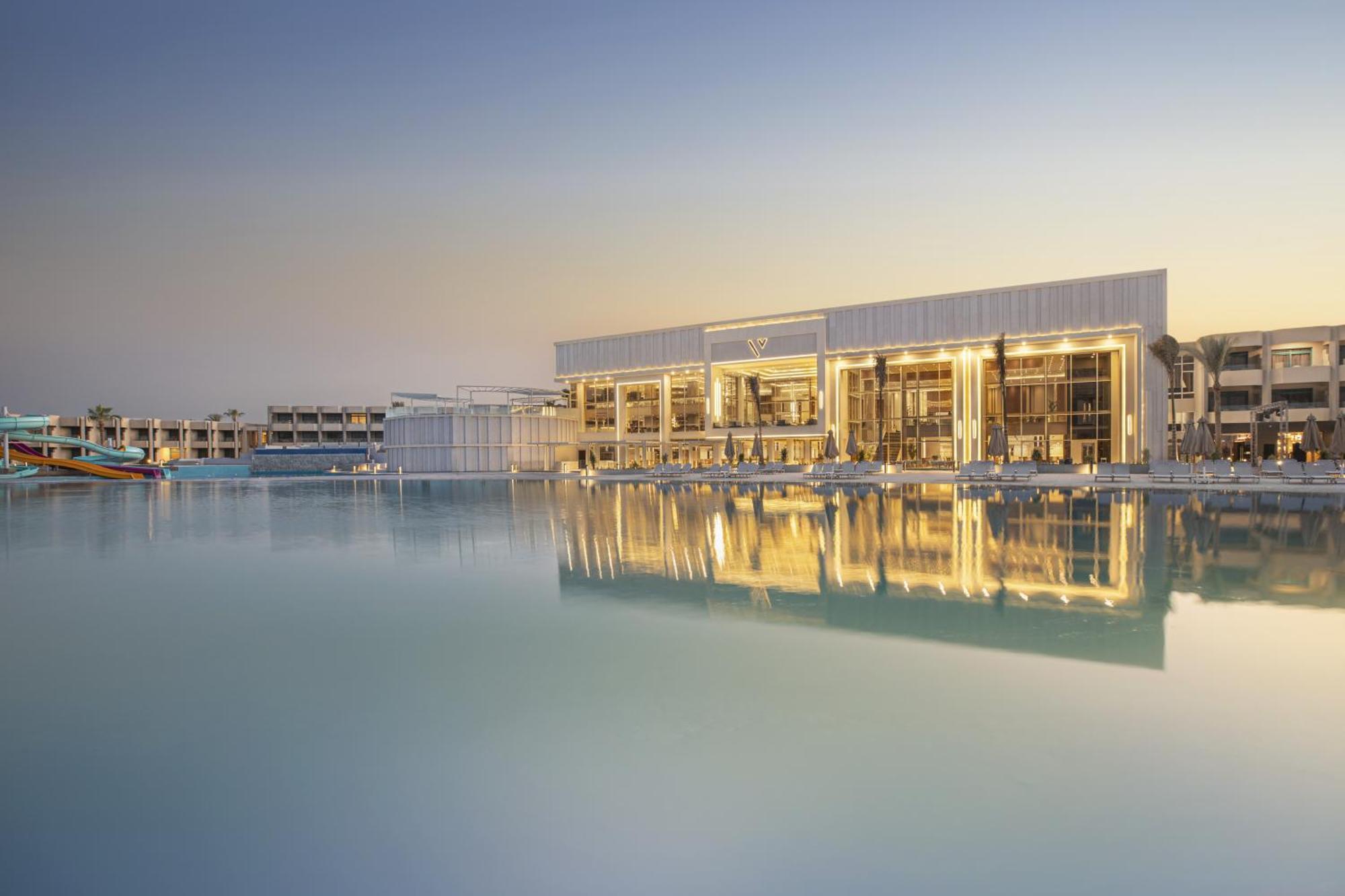 V Hotel Sharm El Shiekh Exterior photo The photo depicts a modern building situated by a calm body of water, likely a lake or lagoon. The structure features a sleek design with large glass windows that reflect the water and the surrounding environment. The setting appears tranquil, possib
