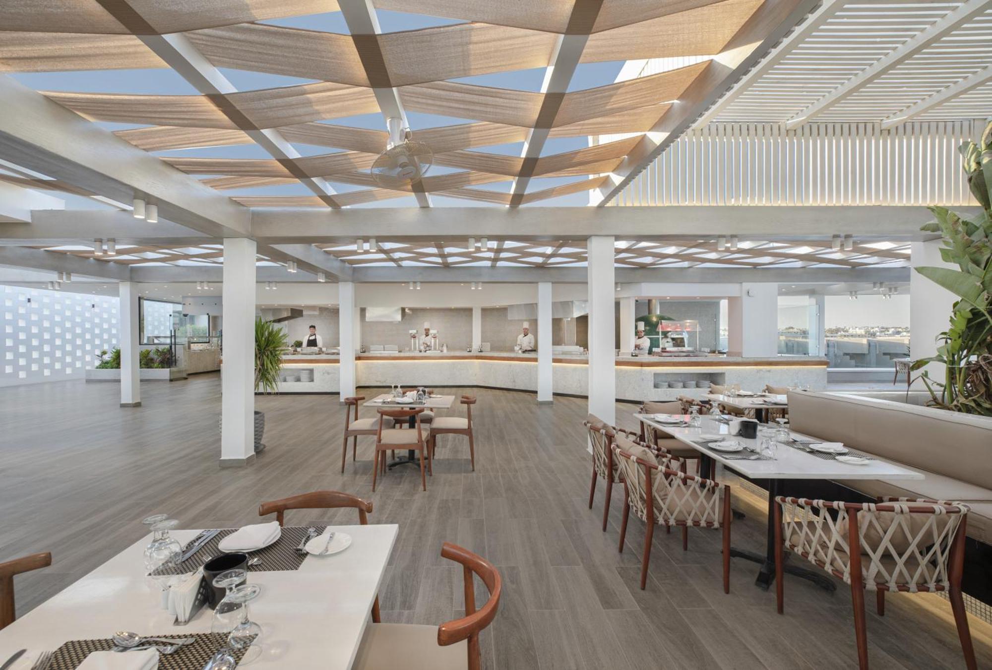V Hotel Sharm El Shiekh Exterior photo The photo shows a modern and spacious restaurant interior. The design features a light and airy atmosphere with large windows allowing for natural light. There are wooden beams in the ceiling, and the floor is made of light-colored wood, contributing